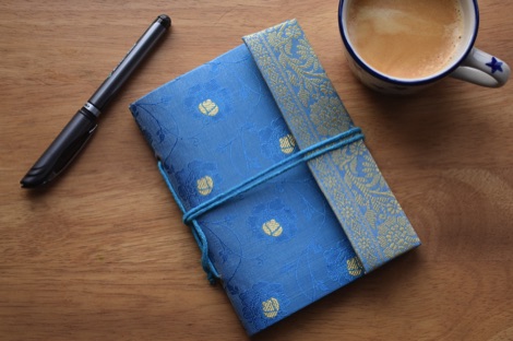 Paper High blue sari-covered notebook on a wooden table with a pen and a cup of coffee